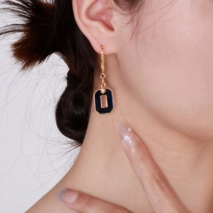 Close-up of elegant gold earrings with deep blue geometric pendant on a female model