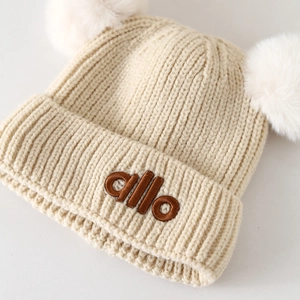 Warme beige Baby-Strickmütze für den Winter mit zwei weißen Pompons und Stickerei