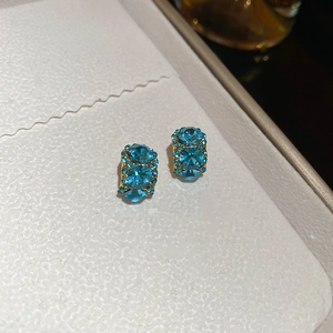 Close-up of 18k gold plated C-shaped earrings with inlaid lake blue faceted gemstones