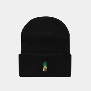 Detail shot of black knitted beanie featuring yellow pineapple embroidery on the folded cuff