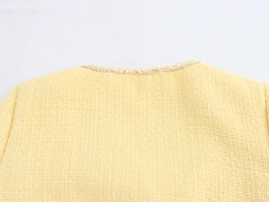 Macro view of the yellow tweed fabric and fringe detail on the dress collar