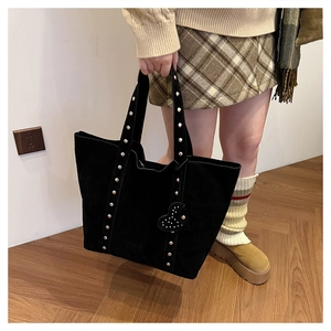 Detail of black suede tote bag featuring silver studs and a heart-shaped rivet charm