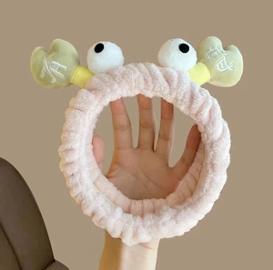 Detail of pink plush crab headband with large eyes and green claws for face washing