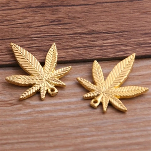 Macro shot of two golden maple leaf metal pendants on a textured wood background