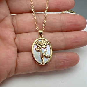 Detailed close-up of a gold oval shell necklace with a 3D floral pendant held by hand