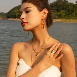 Close-up of vintage gold cross necklaces and earrings on a model with sunset lake background