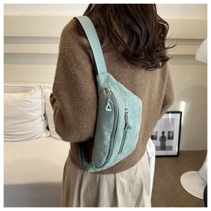 Detail of mint green corduroy crossbody bag worn by a model in a cozy indoor setting