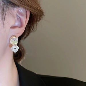 Detail view of flower-shaped pearl earrings with iridescent gemstone on a female model