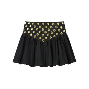 Détail d'une mini-jupe noire avec œillets dorés et ourlet plissé sur un fond blanc pur