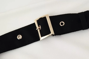Detailed macro view of black woven belt with golden metal buckle and reinforced eyelets
