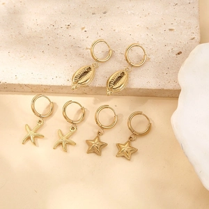 Three pairs of gold hoop earrings with starfish, conch, and star pendants on a stone surface