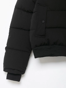Détail d'une veste matelassée noire avec poignets côtelés et poches à bouton-pression