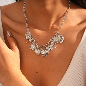 Detail of silver chain necklace with sun, heart, and bow charms on female model