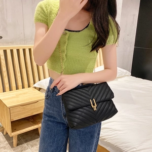Quilted V-pattern shoulder bag in black with gold chain strap on a bedroom scene