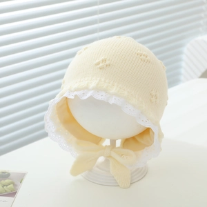 Close-up of beige knit baby hat featuring delicate white lace trim and bow tie detail