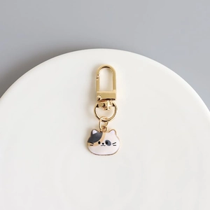 Detail of calico cat enamel charm with gold lobster clasp on white ceramic plate