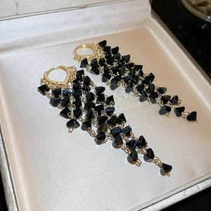 Detailed macro of gold drop earrings featuring tiered black crystal tassels on silk fabric