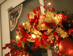 Close-up of red Christmas wreath with poinsettias, berries and warm LED string lights