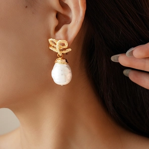 Close-up of vintage baroque pearl earrings with golden bow design on a model
