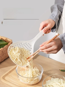 Close-up of a large white Japanese long-handle skimmer ladle draining pasta in a kitchen