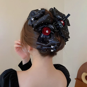 Close-up of a black satin bow hair claw clip with rhinestones and red velvet flower accents