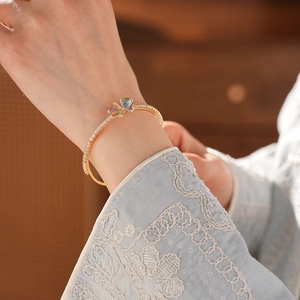 Detail eines goldenen Armreifs mit buntem Zirkonia-Schmetterling am Handgelenk