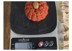 Hand-knitted orange pumpkin decoration weighing 15g on a digital scale for measurement