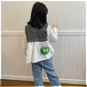 Detail of a green heart-shaped crossbody bag with a cute bow on a girl's outfit