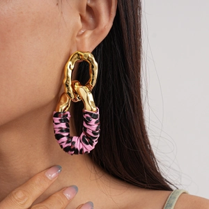 Close-up of golden oval earrings with pink and black zebra print leather texture
