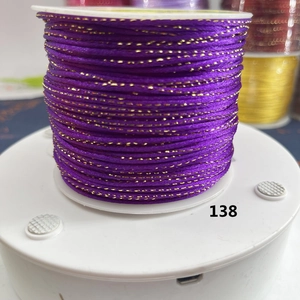 Macro shot of dark purple cord with gold metallic silk thread on a white spool
