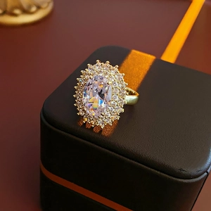 Macro detail of gold-plated oval zircon ring with double halo setting on a black gift box