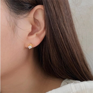 Macro close-up of a minimalist gold bow earring with a sparkling zircon stone on an ear