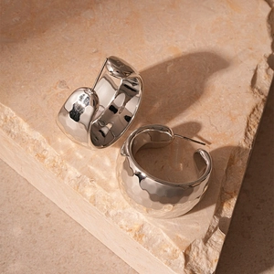 Detail of silver C-shaped stud earrings with hammer texture on a stone background