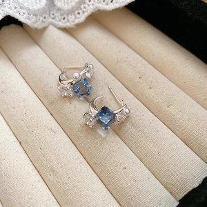 Detailed close-up of blue square zircon earrings with pearls in a beige velvet jewelry box