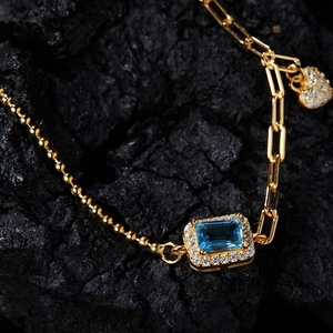 Macro shot of gold bracelet with blue rectangle gemstone and heart-shaped diamond charm