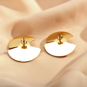 Detail view of golden geometric earrings on elegant beige textured silk fabric backdrop
