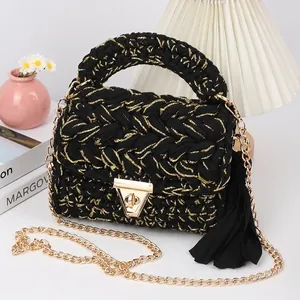 Detail of hand-woven black knit crossbody bag with golden lock and tassel charm