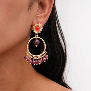 Detail shot of bohemian tassel earrings with purple beads and red stone on a model