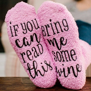 Pink coral fleece socks with black text on soles shown on a warm wooden surface