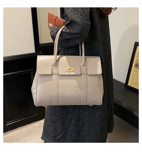 Detailed close-up of beige leather tote with iconic golden postman's lock buckle