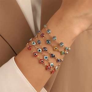 Close-up of stacked colorful Evil Eye bracelets with gold chains on a model's wrist