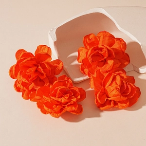 Detailed macro view of four bright orange fabric floral petal earrings on beige background