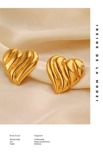 Détail de boucles d'oreilles cœur dorées avec texture ondulée sur soie beige doux