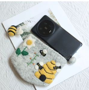 Detailed shot of handmade wool felt bee coin purse used as a smartphone storage pouch