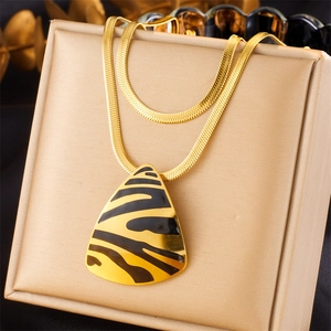 Detail of gold snake chain necklace with a zebra pattern triangle pendant on a beige box