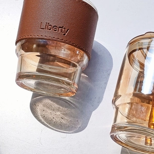 Amber glass bamboo coffee cup with brown leather sleeve and lid in natural light setting