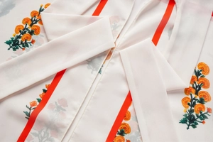 Détail du tissu en mousseline blanche avec motifs floraux oranges et rayures rouges