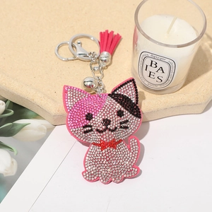 Close-up of pink crystal cat keychain with red tassel, silver bell and metal hook