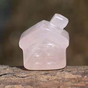 Macro shot of a pink rose quartz house carving placed on a rustic wood surface