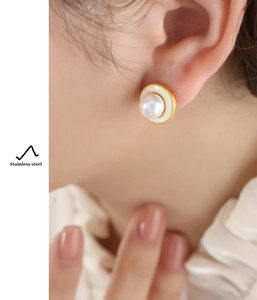 Detail of elegant gold stainless steel stud earrings with pearls worn by a model